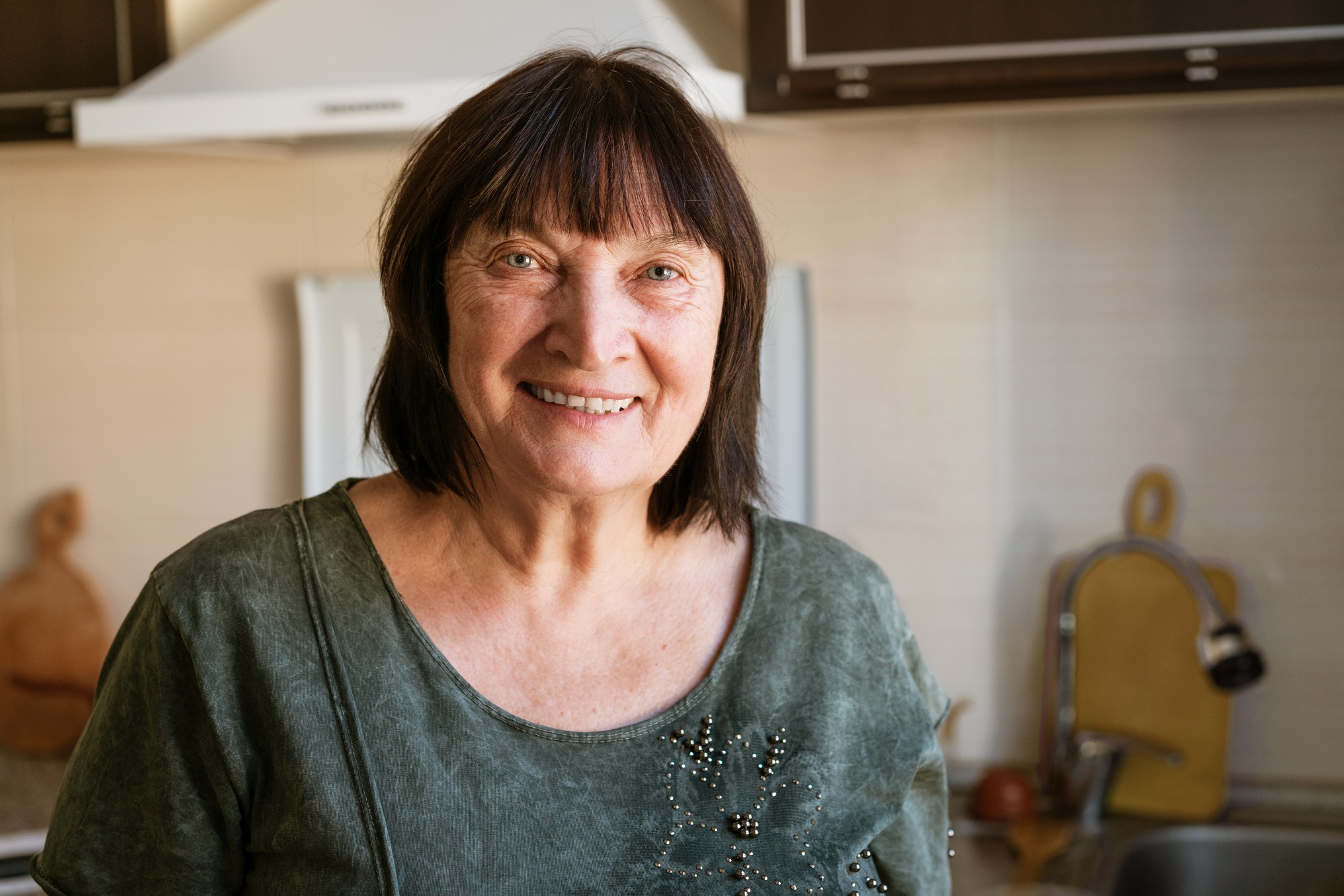 Portrait of happy senior lady sitting in kitchen at home, close-up, copy space.